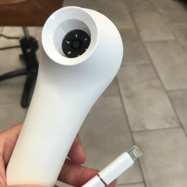 Hand holding white ScalpCam scalp analysis device with cable, used for at-home scalp inspection, dandruff detection, and hair root analysis.