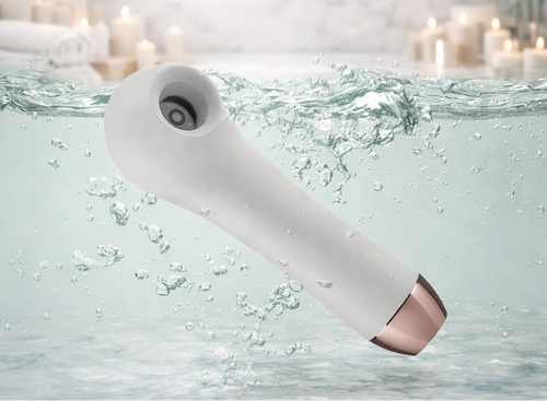 White waterproof ScalpCam scalp analysis device submerged in water with candles in the background, showcasing a water-resistant tool for scalp inspection, dandruff detection, and scalp health monitoring at home or in salons.